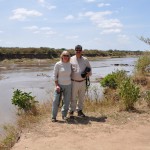 Kathy and Curtis stand on the banks of the Mara River